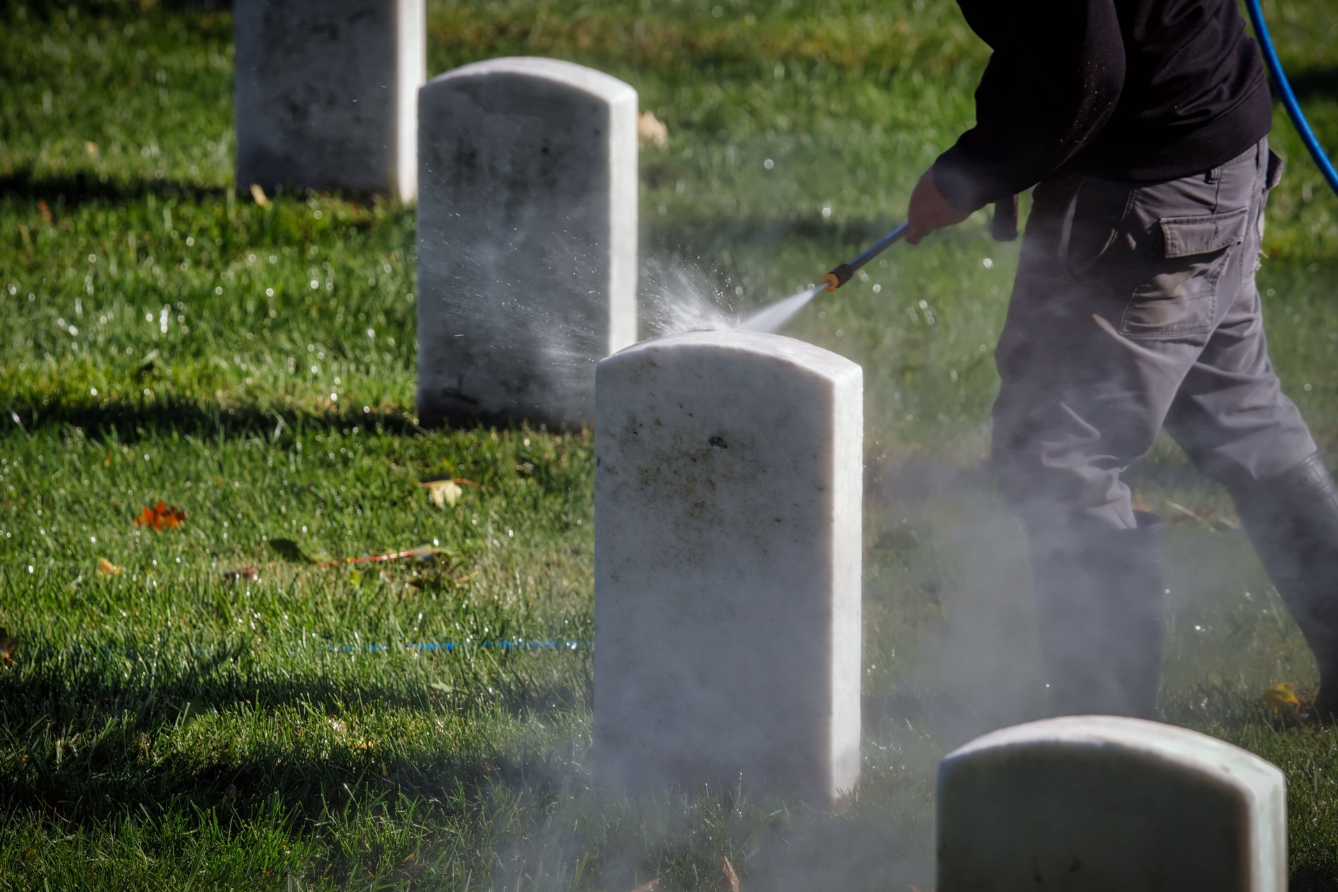 Cleaning headstones with sprayer in cemetery